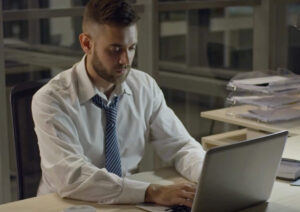 A man sitting slightly hunched forward looking down at a laptop demonstrating posture of tech neck